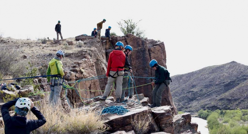 a group of people in rock climbing gear prepare to rappel down a rock face in texas